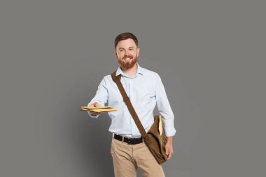 Kahverengi çantalı postacı gri arka planda mektuplar getiriyor.