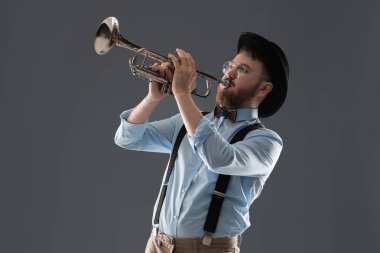 Gri arka planda trompet çalan yakışıklı müzisyen