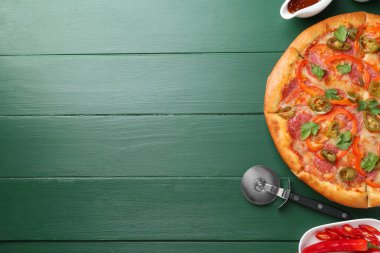 Lezzetli pizza Diablo, sos, taze biber ve yeşil ahşap masa üzerinde makas, düz yatak. Metin için boşluk