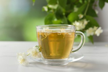 Aromatik yasemin çayı fincanda, çiçekler ve yeşil yapraklar beyaz masada