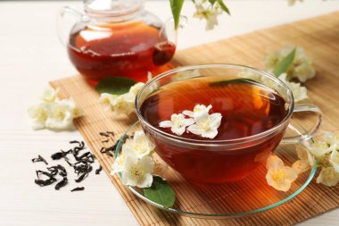 Sıcak yasemin çayı fincanda ve çiçekler beyaz ahşap masada.