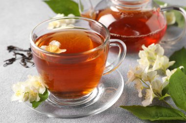 Sıcak yasemin çayı fincanda ve çiçekler açık gri masada.