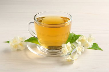 Sıcak yasemin çayı fincanda ve çiçekler beyaz ahşap masada.