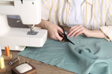 Terzi kadın içeride ahşap masada kumaş kesiyor, yakın plan.