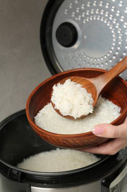 Gri arka planda kaynamış pirinci kaseye koyan kadın, yakın plan.