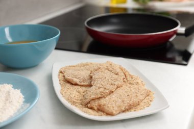 Making schnitzels. Raw meat with bread crumbs on white table, closeup clipart