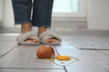 Gri ahşap zeminde, kırılmış çiğ yumurtaya yakın bir kadın, seçici bir odak.