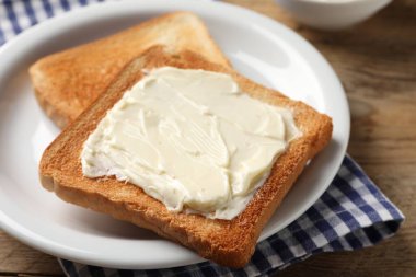 Ahşap masada tereyağlı lezzetli kızarmış ekmek dilimleri, yakın plan.