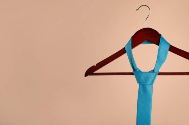 Açık kahverengi arka planda turkuaz kravatlı bir askı. Metin için boşluk