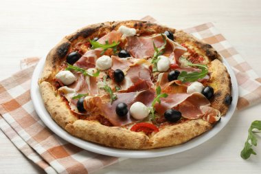 Pişmiş jambon, zeytin, mozarella peyniri, güneşte kurutulmuş domates ve açık ahşap masada roka ile lezzetli bir pizza.