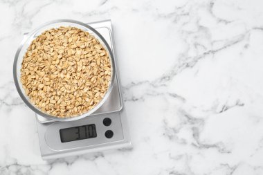 Beyaz mermer masa üzerinde bir kase kuru yulaf ile mutfak terazisi, üst manzara. Metin için boşluk