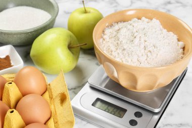 Mutfak terazisi, bir kase un ve beyaz mermer masa üzerindeki ürünler, yakın plan.