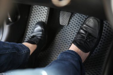 Man in black shoes pushing on pedal of car brake, closeup clipart