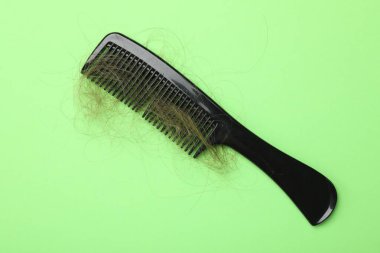 Açık yeşil arka planda saçı dökülmüş bir tarak, üst manzara. Alopecia sorunu