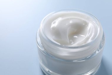 Açık mavi arka planda kavanozda yüz kremi, yakın plan. Metin için boşluk