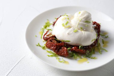 Lezzetli burrata peyniri ve güneşte kurutulmuş domatesler beyaz masada, yakın plan.