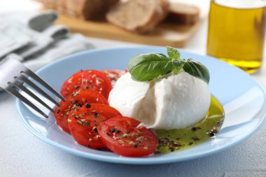 Lezzetli burrata peyniri, domates, fesleğen ve ekmek beyaz masada, yakın plan.