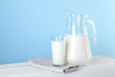 Sürahi ve bir bardak taze süt beyaz ahşap masa üzerinde açık mavi arkaplan, metin için yer