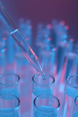 Renk arka planında pipetten test tüpüne sıvı damlatılıyor, yakın plan