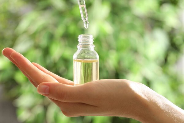Woman dripping essential oil into bottle on blurred background, closeup