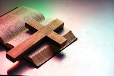 Wooden cross and Bible on textured table in color lights, closeup with space for text. Religion of Christianity clipart