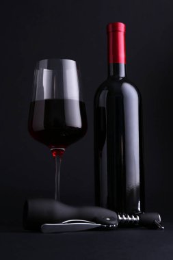 Kanat tirbuşonu, cam ve arka planda kırmızı şarap şişesi.