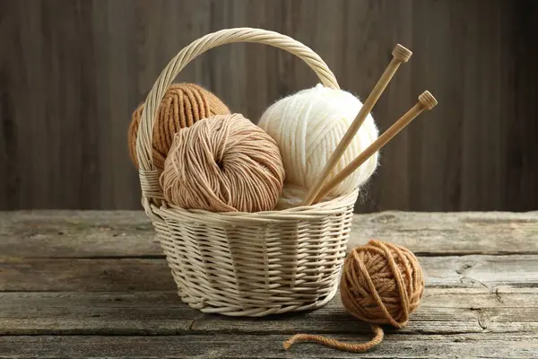 stock image Skeins of yarn, knitting needles and wicker basket on wooden table, closeup