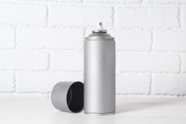 Beyaz tuğla duvarın yanındaki tahta masada sprey boya kutusu.