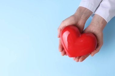 Doktor açık mavi arka planda kırmızı kalbi tutuyor. Metin için boşluk