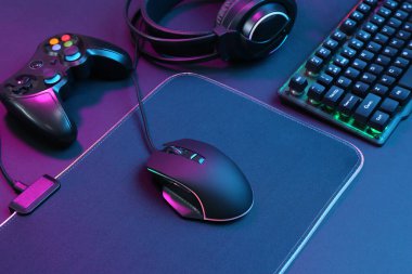 Bilgisayar faresi, RGB klavyesi, oyun denetleyici ve koyu arkaplanda neon ışıkları olan kulaklık