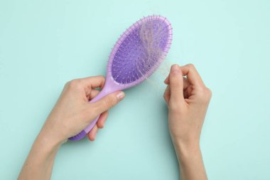 Kayıp saçlarını açık mavi arka planda fırçadan alan kadın, üst manzara. Alopecia sorunu