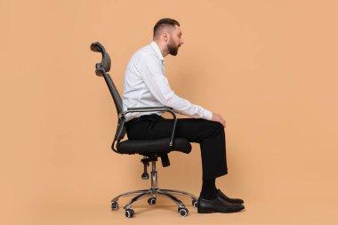 Man with poor posture sitting on chair against pale orange background clipart