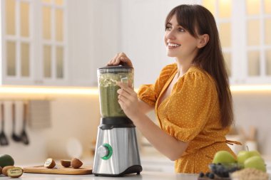 Genç bir kadın mutfaktaki beyaz mermer masada blender ile nefis smoothie yapıyor.