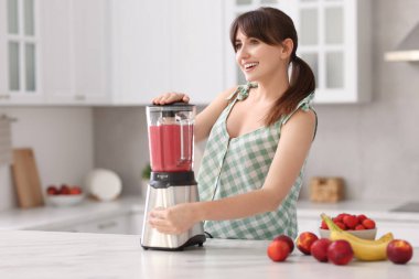 Genç bir kadın mutfaktaki beyaz mermer masada blender ile nefis smoothie yapıyor.