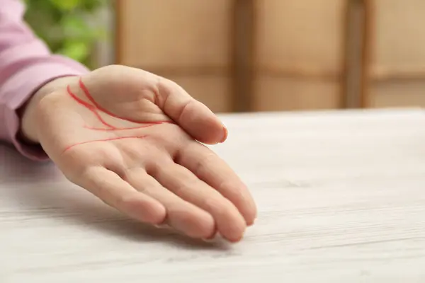 stock image Chiromancy and foretelling. Woman showing palm with drawn lines at white wooden table, closeup. Space for text