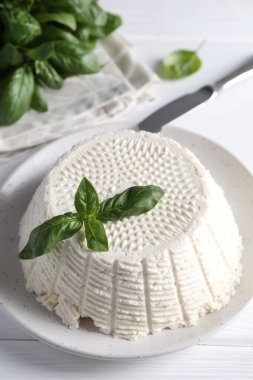 Lezzetli ricotta (krem peynir), beyaz ahşap masada bıçak ve fesleğen, yakın plan.