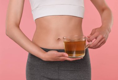 Kilo verme konsepti. Pembe arka planda bir fincan diyet çayı olan kadın, yakın plan.