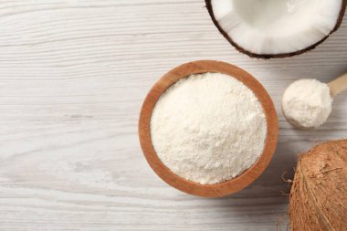 Kâsede taze hindistan cevizi unu, beyaz ahşap masada kaşık ve fındık, düz uzanış. Metin için boşluk