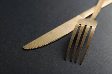 Siyah arka planda zarif altın çatal bıçak takımı, yakın plan.