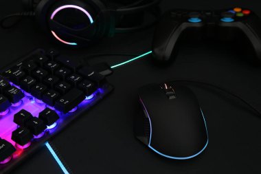 Bilgisayar faresi, RGB klavyesi, kulaklık ve oyun denetleyicisi koyu arkaplanda, yakın plan