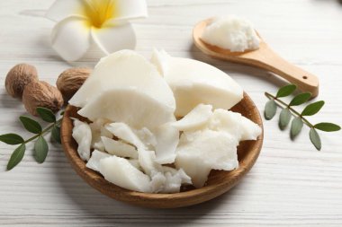 Doğal Shea yağı, fındık, plumeria çiçeği ve ahşap masa üzerindeki yeşil yapraklar.