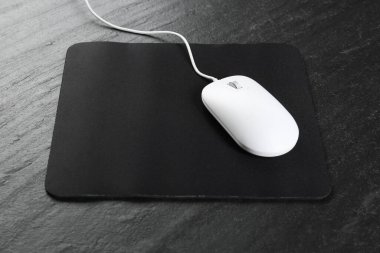 White wired mouse and mousepad on black textured table clipart