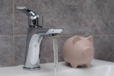 Su tasarrufu konsepti. Banyodaki musluktan akan domuz kumbarası ve su akıntısı, seçici odaklanma