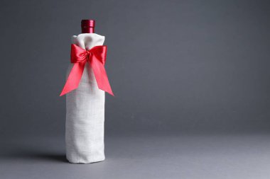 Gri arka planda kırmızı kurdeleli çuval bezi paketinde şarap şişesi, metin için yer
