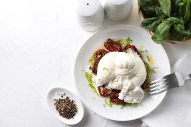 Beyaz masada servis edilen lezzetli burrata peyniri ve güneşte kurutulmuş domatesler. Metin için boşluk