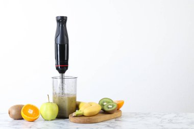 Malzeme karışımı ile el blenderi ve beyaz mermer masa üzerinde taze meyve, metin için yer