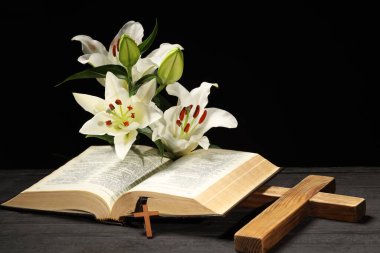 Bible, crosses and lilies on dark gray wooden table against black background. Religion of Christianity clipart