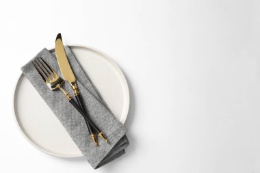Altın çatal bıçak takımı, beyaz arka planda tabak ve peçete, üst manzara. Metin için boşluk