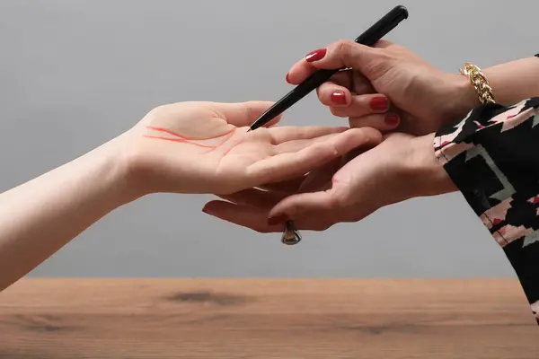 stock image Fortune teller reading lines on woman's palm at wooden table, closeup. Chiromancy