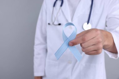 Prostat kanseri farkındalığı. Gri arkaplanda açık mavi kurdele tutan doktor, yakın plan.